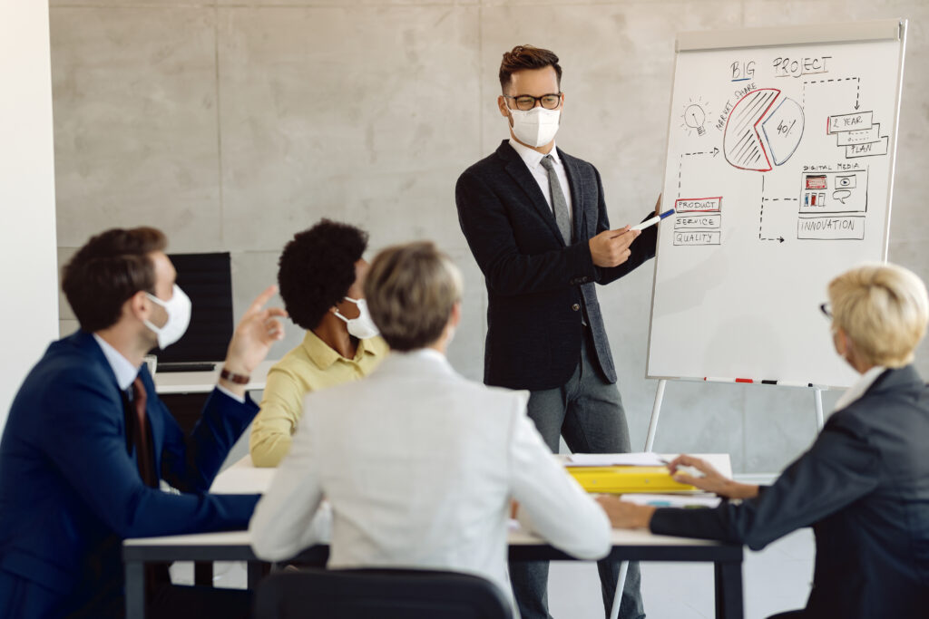 male entrepreneur with face mask giving business presentation his coworker office